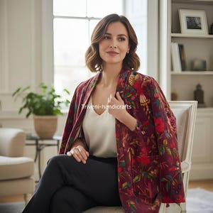 May include: Burgundy floral print jacket with a vibrant bird and flower design. The jacket is worn over a white top and black pants. The text "Triveni-handicrafts" is visible on the jacket.