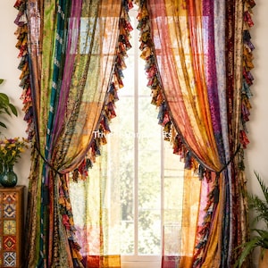 May include: A pair of floor-length curtains made from vertical panels of multicolored, semi-sheer fabric. The curtains feature a patchwork design with various floral and geometric patterns in shades of green, yellow, orange, purple, and red, finished with ruffled edges.