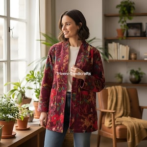Puede incluir: Chaqueta burdeos con estampado floral y dos bolsillos delanteros. La chaqueta tiene un corte holgado y está abierta por delante. El texto "Triveni-handicrafts" está impreso en la chaqueta. La chaqueta se lleva sobre una camiseta blanca y unos vaqueros azules.