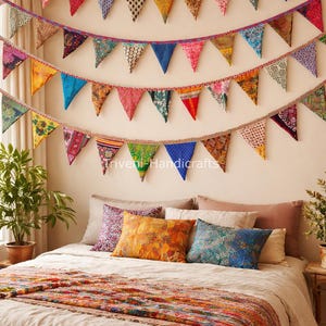 Puede incluir: Una escena de dormitorio con banderines triangulares de tela colorida colgados sobre una cama. La cama tiene almohadas estampadas y una colcha decorativa. El texto "Triveni Handicrafts" es visible en la pared.