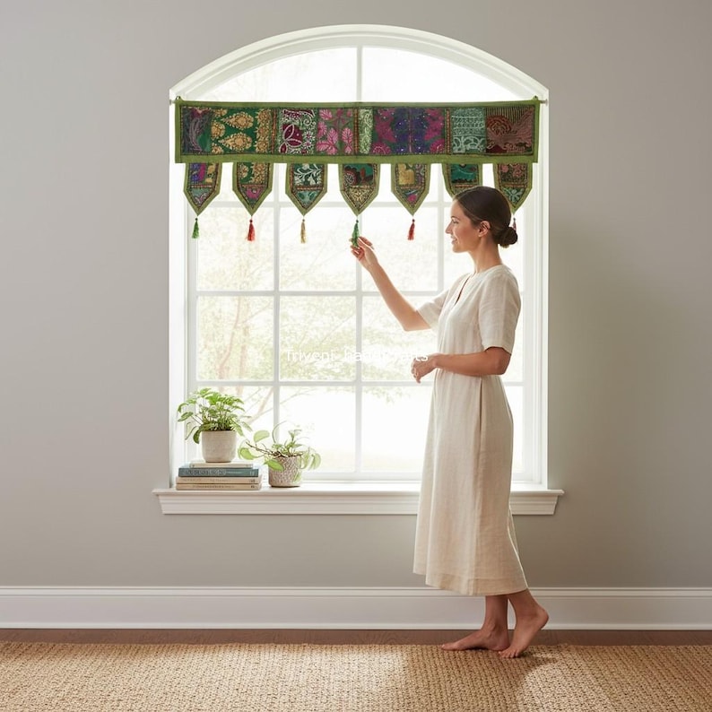 May include: A green and multi-colored window valance with a floral pattern is displayed above a window. The valance has a series of decorative panels and hanging tassels. The window has a white frame and is letting in natural light.