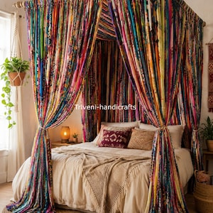 Op de afbeelding: Een hemelbedframe gedrapeerd met levendige, veelkleurige stoffen stroken in diverse patronen. De hemelgordijnen bevatten een mix van heldere tinten, waaronder rood, blauw, geel en groen. De tekst Triveni-handicrafts is zichtbaar.