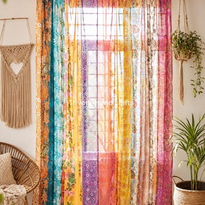 May include: A sheer window curtain featuring vertical panels of vibrant, multi-colored fabric with intricate floral and geometric patterns. The curtain hangs from a dark rod with fabric loops and displays the text Triveri Handcrafts.