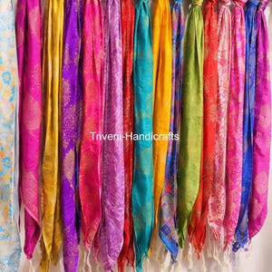 May include: A collection of colorful scarves hanging from a rod. The scarves are in various shades of pink, purple, yellow, red, green, and blue. The text "Triveni-Handicrafts" is visible on the scarves. The scarves have a patterned design.