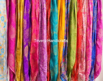 May include: A collection of colorful scarves hanging from a rod. The scarves are in various shades of pink, purple, yellow, red, green, and blue. The text "Triveni-Handicrafts" is visible on the scarves. The scarves have a patterned design.