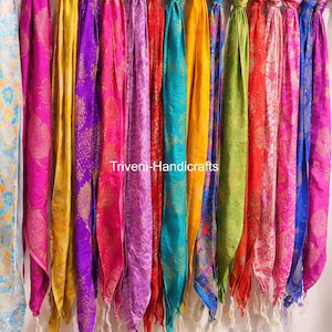 May include: A collection of colorful scarves hanging from a rod. The scarves are in various shades of pink, purple, yellow, red, green, blue, and turquoise. The text "Triveni-Handicrafts" is visible on the scarves.