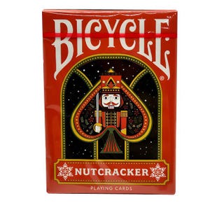 May include: A red Bicycle playing card deck with a nutcracker theme. The spade-shaped card face features a nutcracker soldier illustration. The box displays the text "Bicycle", "Nutcracker", and "Playing Cards".