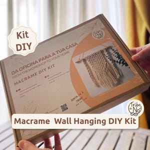 Op de afbeelding: Een rechthoekige kartonnen doos voor een macramé wandhanger doe-het-zelfpakket. De doos bevat een perzikkleurige afbeelding, een foto van een afgewerkt macraméstuk en tekst waaronder "Kit DIY", "MACRAME DIY KIT" en "Macrame Wall Hanging DIY Kit."