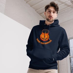 Könnte beinhalten: Marineblauer Kapuzenpullover mit einem Kürbis-Laternen-Design und einem Kettlebell-Griff sowie dem Text "Smash Your Pumpkins" in Orange. Der Aufdruck befindet sich auf der Vorderseite. Der Hoodie hat eine Vordertasche und eine Kapuze mit Kordelzug.