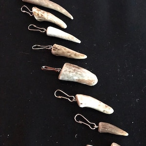 May include: Nine antler keychains with silver rings. Each keychain is a different size and shape. The antler keychains are all natural and have a light brown color.