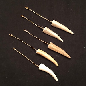 Może przedstawiać: Pięć białych łańcuszków do ciągnięcia wentylatora z poroża z złotymi łańcuszkami. Pociągające elementy z poroża są różnych rozmiarów i kształtów.