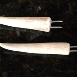 Puede incluir: Dos pinchos de asta de ciervo blanca con dos puntas en cada extremo. Los pinchos están hechos de asta de ciervo natural y tienen un acabado liso y pulido.