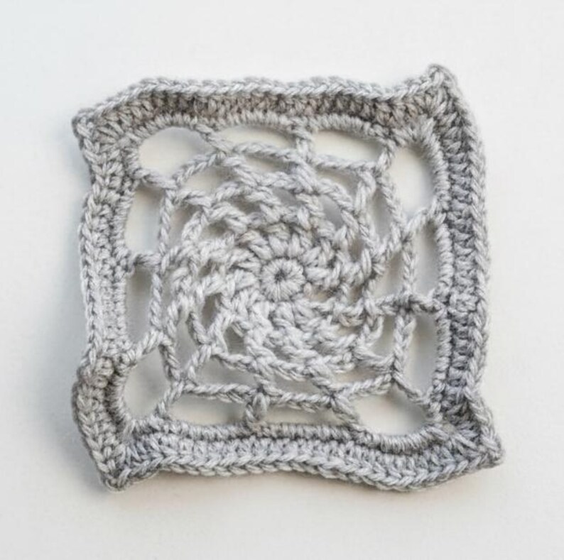 May include: A square, crocheted doily in shades of gray. The center features a spiral design, surrounded by an open, web-like pattern. The edges are finished with a solid, textured border. The handmade piece is displayed on a white surface.