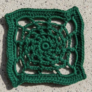 May include: A square, handmade crochet doily in a deep forest green. The center features a spiral design, surrounded by an open, lacy pattern within a solid border. The yarn appears thick and textured.