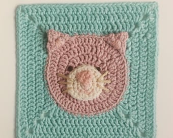 May include: A square crochet pattern featuring a cat's face. The cat's face is pink with a white muzzle and brown eyes, set against a light blue background. The text "Cat Crochet Pattern" is at the top.