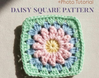 May include: A square crochet pattern featuring a daisy design. The center of the daisy is yellow, surrounded by pink petals, blue, and a green border. The text "DAISY SQUARE PATTERN" is at the top.