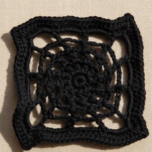 May include: A square, black crochet doily with an open, web-like design. The doily features a spiral center and a solid, textured border. The intricate pattern is visible against a neutral background, highlighting the handmade quality of the piece.