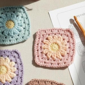 May include: Close-up of several crocheted squares in pastel colors, each featuring a flower design. A wooden crochet hook and a pattern sheet with the text "myrsh dam" are also visible. The squares are in shades of blue, pink, purple, and brown.