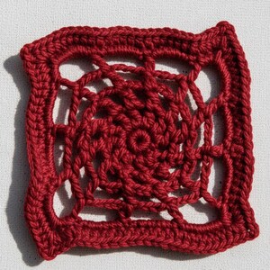 May include: A square, openwork crochet doily in a deep red hue. The design features a central spiral pattern surrounded by an open, geometric border. The handmade piece is displayed on a white surface.