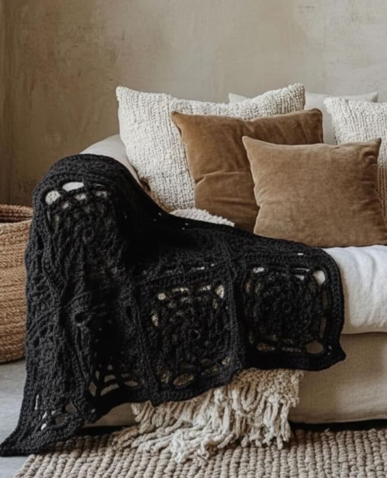 May include: A black, crocheted blanket draped over a sofa with brown and white pillows. The blanket has a geometric pattern with openwork squares. A woven basket is visible on the left.
