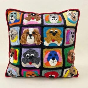 May include: A square crochet pillow featuring a patchwork design of various dog breeds. Each square showcases a different dog face with detailed features and vibrant colors. The pillow has a red border.