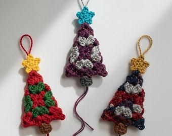 May include: Three handmade crochet Christmas tree ornaments. Each tree is a different color scheme: red and green, purple and gray, and red, white, and blue. Each tree has a star on top and a loop for hanging.