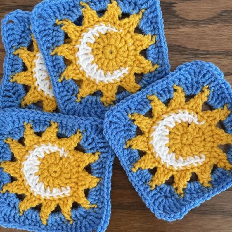Pode incluir: Quatro quadrados de croch&ecirc; feitos &agrave; m&atilde;o em azul, amarelo e branco. Cada quadrado apresenta um desenho de sol e lua crescente. Os quadrados s&atilde;o dispostos em um padr&atilde;o ligeiramente sobreposto, mostrando o intrincado trabalho de croch&ecirc;.