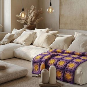 May include: A cozy living room scene featuring a modular sofa with cream-colored cushions and pillows. A vibrant, hand-crocheted blanket in purple and yellow adds a pop of color. Decorative elements include pendant lights and dried plants.