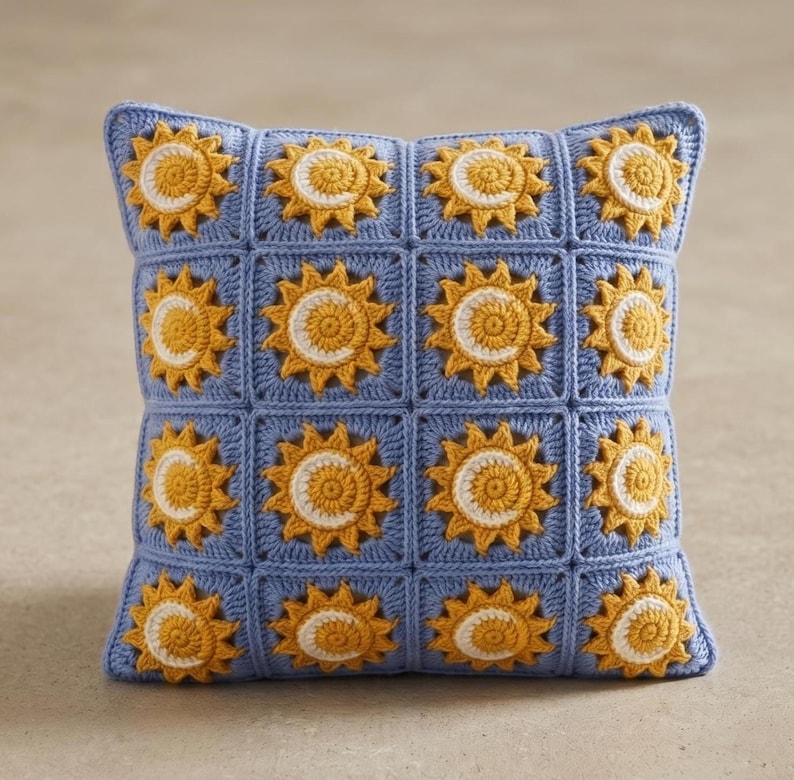 Pode incluir: Uma almofada quadrada de croch&ecirc; com fundo azul e um padr&atilde;o de s&oacute;is amarelos e brancos. A almofada &eacute; feita de quadrados individuais, cada um com um desenho de sol. A almofada tem aproximadamente 40 cm quadrados.