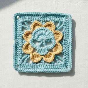 May include: A square, crocheted doily featuring a skull design. The skull is light blue, surrounded by a golden-yellow flower shape, and set against a light blue square background. The handmade item is likely for home decor.