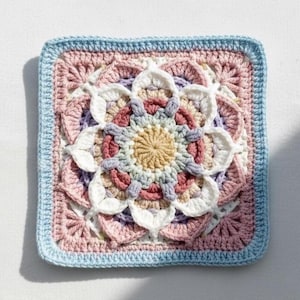 May include: A square, hand-crocheted item with a floral pattern. It has a light blue border, enclosing a central flower with white, pink, and purple petals. The flower's centre is a light yellow colour.