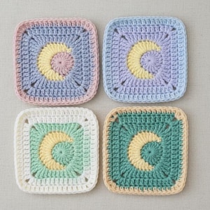 May include: Four square crochet coasters in pastel colors. Each coaster features a crescent moon design in yellow, with a different color scheme: pink and blue, purple and blue, green and white, and teal and beige.