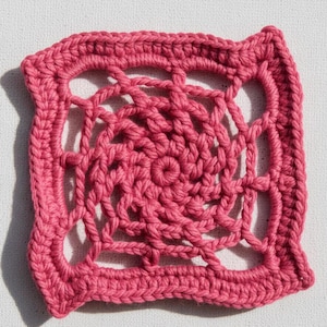 May include: A square, handmade crochet doily in a vibrant shade of pink. The design features a central spiral pattern surrounded by an open, web-like structure. The edges are neatly finished with a solid border, showcasing the intricate craftsmanship.