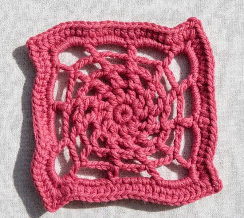 May include: A square, handmade crochet doily in a vibrant shade of pink. The design features a central spiral pattern surrounded by an open, web-like structure. The edges are neatly finished with a solid border, showcasing the intricate craftsmanship.