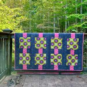 Puede incluir: Una colcha con fondo azul oscuro y patrones florales rosas y amarillos. La colcha está colgada en una barandilla de madera.