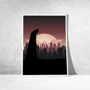 Op de afbeelding: Een ingelijste kunstdruk met een silhouet van Batman met uitzicht op een stadsgezicht. Het kunstwerk heeft een donker kleurenpalet met een rood-zwarte gradiënthemel, een groot Batman-symbool en een gedetailleerde skyline.