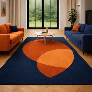 May include: A contemporary living room with a navy blue rug featuring two orange shapes. Two orange sofas and a blue sofa surround a round wooden coffee table. The room has large windows and beige curtains.