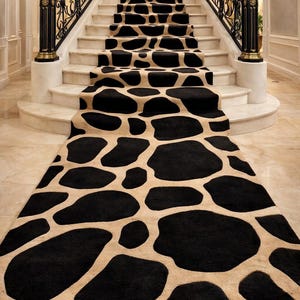 Peut inclure: Un tapis de couloir pour escalier à motifs noirs et beiges. Le tapis présente un motif répété de grandes formes noires irrégulières sur un fond beige. Le tapis est installé sur un escalier en marbre avec des rampes noires et dorées ornées.