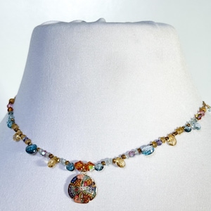 Könnte beinhalten: Eine farbenfrohe Halskette mit einem Anhänger in Form eines Sanddollars. Die Halskette hat blaue, gelbe, orangefarbene und violette Perlen. Der Sanddollar-Anhänger ist mehrfarbig mit einem Sternmuster.