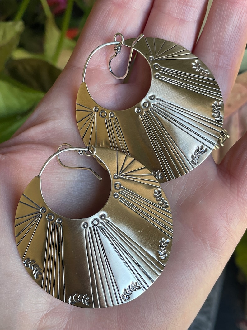 May include: A pair of silver hoop earrings with a sunburst design and leaf accents.