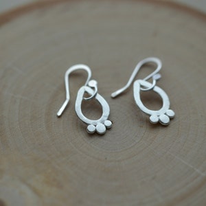 May include: A pair of silver dangle earrings with a teardrop shape and small circles at the bottom.