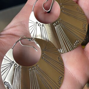 May include: A pair of silver hoop earrings with a sunburst design and small leaf accents.