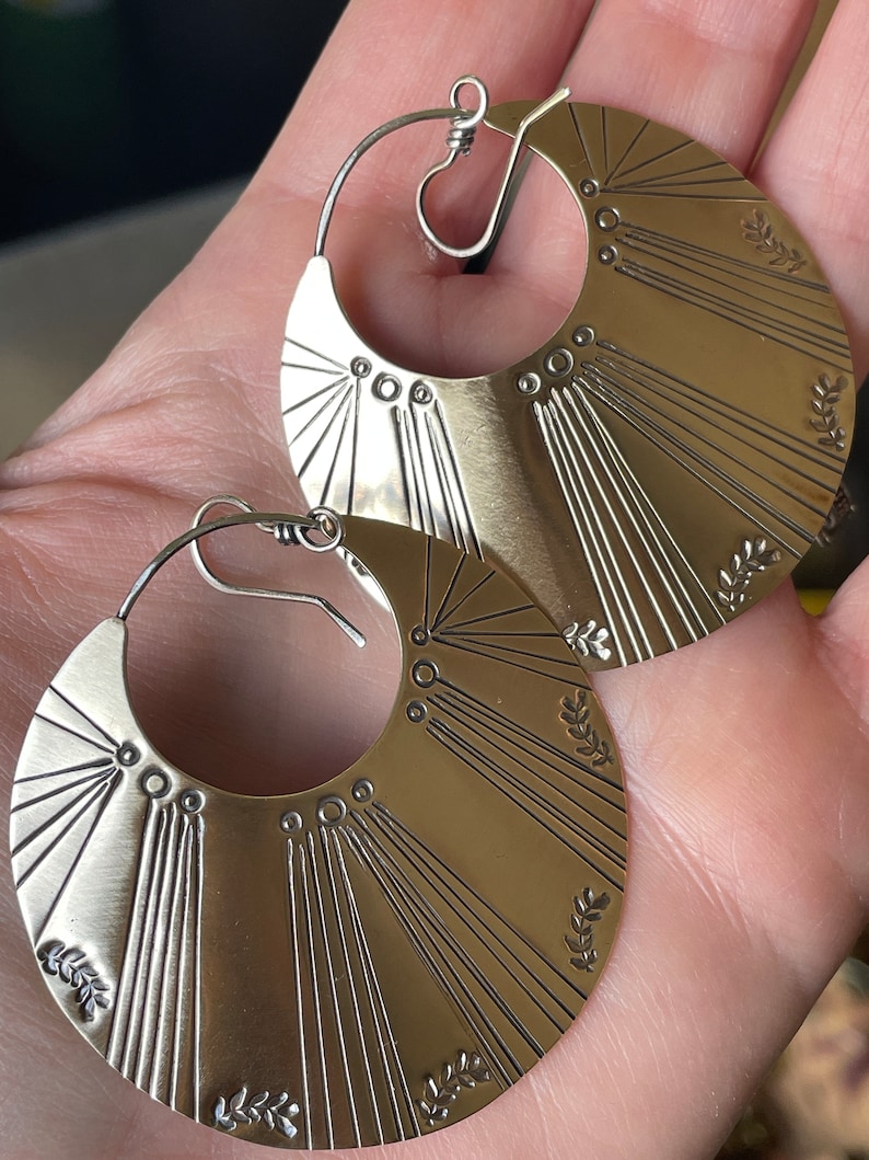 May include: A pair of silver hoop earrings with a sunburst design and small leaf accents.