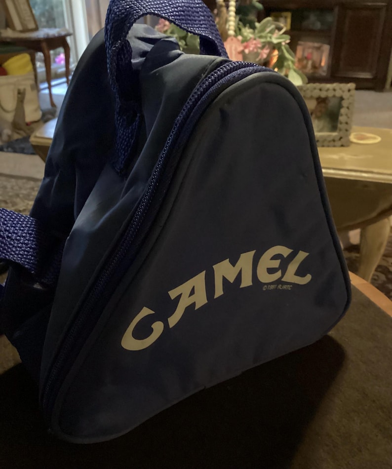 May include: A navy blue triangular bag with a zipper closure and a handle. The bag features the word "CAMEL" in a stylized font. The bag is made of a durable material and has a simple design.