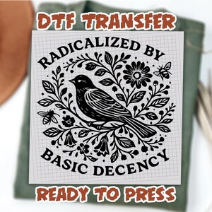 May include: A black and white DTF transfer with the text "RADICALIZED BY BASIC DECENCY" and a detailed illustration of a bird perched on a branch surrounded by flowers and leaves. The words "READY TO PRESS" are also included.