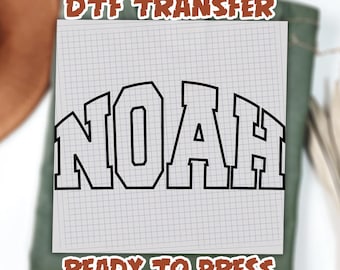 May include: A DTF transfer with the name "NOAH" in a bold, black, collegiate-style font. The transfer is on a grid-lined paper, with the text "DTF TRANSFER" and "READY TO PRESS" in a brown, outlined font.