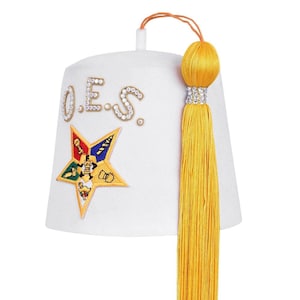 Puede incluir: Gorro fez blanco con las letras "O.E.S." en pedrería. Una borla amarilla cuelga del lateral. La parte delantera del sombrero presenta un emblema de estrella colorido con varios símbolos y figuras.