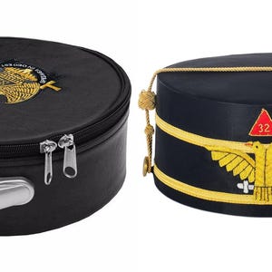 Puede incluir: Se muestran dos sombreros. Uno es un estuche de sombrero negro y redondo con cremallera y asa, con un emblema dorado. El otro es un sombrero azul marino con ribete dorado, un triángulo rojo con el número 32 y un emblema dorado.