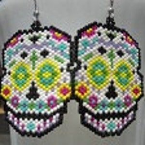 May include: A pair of large, colorful, beaded sugar skull earrings. The earrings are white with black outlines and feature a variety of colors, including pink, purple, green, yellow, and blue. The earrings are shaped like sugar skulls, a traditional Mexican symbol of Day of the Dead.