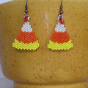 May include: A pair of candy corn earrings made with white, orange, and yellow beads. The earrings are hanging from bronze hooks.